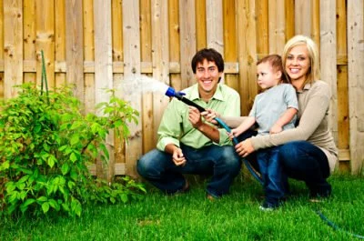 family watering plants by a wooden vinyl aluminum fence around a house